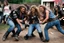 Placeholder: two heavy ahtletic muscular teenage-biker-girls rolling on the ground while furiously scuffling & headlocking each other and pulling hair in a crowd in a yard with grafitti. All wearing dirty washy Bluejeans pants with broad leather belts with huge buckles & studded hipbelts & dirty t-shirts & dirty shabby biker-leather-jackets with club-patches & dirty biker-overknees. epic tv-fight-scene.