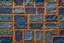 Placeholder: leather background covered with a grid of many different sized rectangular weathered and faded denim patches (navy blue) that are each stitched (brown) and nailed (brass) around the edges