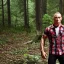 Placeholder: georges st pierre with a red plaid shirt, a backpack and a rifle in a creepy forrest with zombies