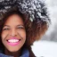 Placeholder: portrait of a black woman with realistic facial features, perfect smile, and brown coily hair in winter wonderland