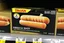 Placeholder: satirical product advertisement, Trojan brand black and gold sandwich bag box on display on a grocery store shelf, "RIBBED SANDWICH BAGS", picture on box is a long tubular hot dog bun poking out of an opaque yellow crenelated plastic bag, photorealistic, HD, natural lighting, Trojan brand logo