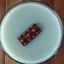 Placeholder: grainy photography, top-down perspective, large glass punchbowl full of light blue punch on a wooden table with a chocolate log candy bar floating in the bowl,