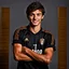 Placeholder: 85mm DSLR color photography of a very detailed headshot fitting all of head and hair in frame. 18-year-old Italian soccer player, with brown hair color and no facial hair and has very short hair and with a small smile, grey background make him look like he has Spanish origins