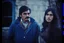 Placeholder: ayoung man and a beautiful woman standing next to each other, 1 9 7 0 s analog video, with mustache, assyrian, small glasses, cold scene, out of focus background, house on background, the woman has long dark hair, the photo shows a large, deiv calviz, before the final culling