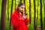 Placeholder: young woman in red clothing standing in a forest holding a smartphone