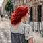 Placeholder: a girl with bright red hair, looking over her shoulder, walking along a bust street