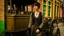 Placeholder: body portrait of a gothic woman with a black bob with a full fringe hairstyle, dressed in brown leather trousers, waistcoat, and gloves, in a Victorian street next to a steam carriage, full colour