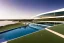 Placeholder: Sunset algarve in quinta do lago, one straight line building of 250 meters long pool of a modern luxury architecture with wood and gold metallic pergolas with pool on rooftop, with green roofs and sun loungers next to pool, overlooking a tennis and padel sport facility and inserted in the Ria Formosa Natural park, on a slope with pinus pinea, a wrap around low speed veicular road, aerial view