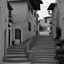 Placeholder: Calle de un pueblo de una isla italiana en verano, con escalinata, fotografía real, fotografía realizada con cámara Leica y objetivo de 50 mm, siguiendo estilo de la serie 'Ripley' emitida en Netflix, fotografía en blanco y negro, virada tonos años 50