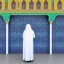 Placeholder: woman in flowing, white burka standing in front of a mosque with blue, green, gold mosaic walls, profile, wide-angle lens, full-body, panoramic, high-quality, fine-detail, intricate, ornate, volumetric lighting, 8k resolution, haunting, powerful, photo-realistic, 3d render, photo-quality, high-quality