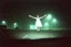 Placeholder: create a low-quality dashboard cam picture, high film grain, ghostly faceless girl in a white dress with arms extended levitating high off ground caught in headlights in an empty Wal-Mart parking lot on a foggy night, found footage, low contrast, super grainy greenish night vision hues, static haze.