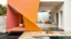 Placeholder: Casa escultórica compuesta por prismas superpuestos en tonos rosa mexicano, amarillo mostaza y blanco calizo, corredores abiertos conectando patios interiores con cactus y vegetación mediterránea contenida, pavimento de piedra natural húmeda tras la lluvia, perro dormido junto a un umbral oscuro, composición minimalista y geométrica, contraste entre superficies rugosas y agua pulida, representación como gouache arquitectónico contemporáneo con sensibilidad de Ricardo Bofill y David Hockney.