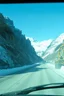 Placeholder: surreal green plastic mountain road seen through a dirty truck front window, dirty blue snow and wind, autochrome