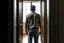 Placeholder: man in jeans and a shirt, back to the camera, standing in a row of doors, looking out through a doorway
