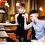 Placeholder: Russian guy student boy boyish boylike short man's haircut men's face boyish features female figure in black girlish lacy cocktail dress earrings in restaurant