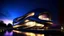 Placeholder: - Museo futurista con formas fluidas, metal reflectante, estilo Zaha Hadid, iluminación dusk dramática.