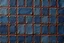 Placeholder: leather background covered with a grid of many rectangular weathered and faded denim patches (navy blue) that are each stitched (brown) and nailed (brass) around the edges