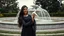 Placeholder: Hyper Realistic Photographic View Of A Beautiful Young Pakistani Pashto Woman (With Beautiful Long Black Hair) Wearing A Beautiful Black Dress With Black Embroidery; Happily Holding A White Pigeon And Standing With Green Grass With A White Marble Water Fountain Behind Her At Beautiful Cloudy Day Showing Dramatic And Cinematic Ambiance.