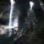 Placeholder: Epic fantasy digital painting of two robed figures, reminiscent of Dante and Virgil in the style of a Gustave Doré engraving, journeying on a perilous stone path carved into the wall of a vast, subterranean underworld. A majestic, luminous waterfall cascades from a sunlit hole in the cavern ceiling, its spray catching the divine light. The rest of the cavern is lost in deep, moody shadows, creating intense chiaroscuro. Moss-covered rocks glisten on the far side of a dark, still river.