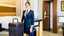 Placeholder: at hotel front desk representative holding suitcase behind back