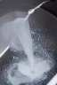 Placeholder: in focus, a jet of water flows into a spoon and splashes everywhere in a sink tray