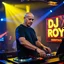 Placeholder: A dj on a night rave club standing mixing songs , he looks like the actor Bryan Cranston, bald man. strobes and blue yellow light, a big sign with "DJ ROY" in the background, this is a album cover for his dj roy assentials album.