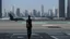 Placeholder: Tall thin woman, with straight black hair, dressed in a camouflaged jumpsuit, looking out from the rear of a futuristic aircar, on a tarmac runway, with a city skyline in the distance