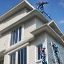 Placeholder: Workers standing on a ladder reaching up onto the edge of a house installing seamless gutters to the fascia