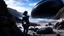 Placeholder: A woman in a catsuit standing on a beach of a rocky landscape with a crashed spaceship in the distance