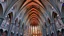 Placeholder: A majestic cathedral with towering hyperbolic arches defining the structure. The roof and walls curve inward and outward in perfect harmony, creating a fluid, wave-like design. The arches are lined with intricate stained glass windows that cast colorful light through the building, adding a sense of ethereal beauty. Award-winning photograph.