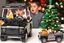 Placeholder: A crying toddler takes a burning car out of a LEGO box marked Land Rover next to the Christmas tree.