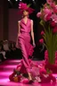 Placeholder: Model in runway with pink orchids like principal elements and element that recall olives trees and palm