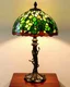 Placeholder: Tiffany-Style Lamp — stained glass shade with peacock feather pattern, bronze vine base, glowing on mahogany desk.