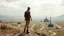 Placeholder: A photorealistic image of a slender 60-year-old woman, in brown shorts, a shirt and boots, with a backpack, standing on a hill looking down on a derelict sci-fi village with low alien buildings.