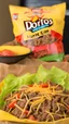 Placeholder: "Taco in a Bag" which consists of an open Doritos chip bag containing Doritos chips and cooked ground beef and lettuce and shredded cheese and tomato pepper and onions and more naco chips, food blogger photography