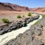 Placeholder: Fotografia di un paesaggio desertico con ruscello con polvere simile a malta e calcina, piante, rocce ruvide scure e corrose dallo scorrere dell'acqia