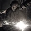 Placeholder: Imagen realista y dramática de una trabajador en una fábrica de fundición rodeado de las chispas que saltan, en medio de la penumbra, primer plano del trabajador mirando la pieza que funde. Fotografía periodística realizada con una cámara Leica y un objetivo de 50 mm