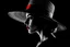 Placeholder: a striking artistic portrait with a dramatic film noir aesthetic. The image shows a woman in profile wearing a wide-brimmed hat, rendered in a high-contrast black and white style with selective red coloring on the hat and lips. The technique creates a textured, almost sketched appearance that gives it an elegant, vintage feel. The composition emphasizes mystery and sophistication - the shadowing obscures most facial details while the red accents draw attention to the hat and lips, creating a bol
