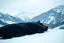 Placeholder: in distance side a wiev a figure in dark clothes and long black leather coat lies on his back in the snow and looks the sky in a winter landscape, alone, white snow, high contrast, cold, winter, mountains, white, blue, gray and black colors, cinematic, atmospheric, dark, gloomy, thriller vibe, crepy stunning