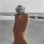 Placeholder: Marilyn monroe with long plaids, in a large orange woollen sweater, on the beach, in the sun, wind