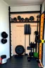 Placeholder: Home gym, wall with a kabinet with weights and small gym equipment. The other side a plyo box and wall balls. In between the plyo box and kabinet a folded weightlifting bench.