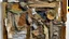 Placeholder: Three-dimensional collage with contrasting textures, worn and torn fabrics in earth tones, aged wood with exposed grain, rusty nails emerging from rough surfaces, abstract biomorphic forms, thick paint spatter, embedded coarse sand, overlapping layers of materials, contemporary material art style