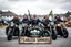 Placeholder: a very hard and tuff motorcycle young gang with Keltic hair , not old, posing with their Harley Davidsson bikes, some of them holding guns and shotguns, a logo sign with "FALKÖPING HD", "FEARLESS SINNERS" Skulls and bones, skeletons and fire, Swedish town Falköping in background, Swedish flags on bikes, Simon Stålenhag style
