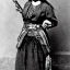 Placeholder: sepia portrait of female mexican outlaw wearing gunbelt holster with guns on waist, bandolier belts with rows of bullets criss-cross chest, long black wavy hair, beautiful face, 1800s, 8k, high-quality, ultra-fine detail,