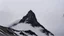 Placeholder: looking up at a single sharp narrow mountain, the peak obscured by clouds and fog.