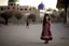 Placeholder: A five-year-old Palestinian girl wearing a traditional dress and new shoes looks to the side and points at a distant building.