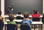 Placeholder: class of children's students, view from the back of the class, looking at the blackboard, students sitting at their desk and a student writing on the blackboard, real photography, reality, photojournalism