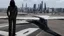 Placeholder: Tall thin woman, with straight black hair, dressed in a camouflaged jumpsuit, looking out from the rear of a futuristic aircar, on a tarmac runway, with a city skyline in the distance