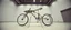 Placeholder: pinhole cam, weird geometry sacred, airbrush 3d rendering, integrated_multimodal_description: [Shot 1] A five-second cinematic single take in a clean industrial presentation hall. A bizarre mechanically plausible bicycle machine stands beside a presentation podium, designed to look like a giant mechanical praying mantis. Two large bicycle wheels form its main body and four thin articulated mechanical legs support it. Two long folded mechanical front arms resemble mantis forelegs.
