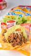 Placeholder: "Taco in a Bag" which consists of an open Doritos chip bag containing Doritos chips and cooked ground beef and lettuce and shredded cheese and tomato pepper and onions and more nacho chips, food blogger photography